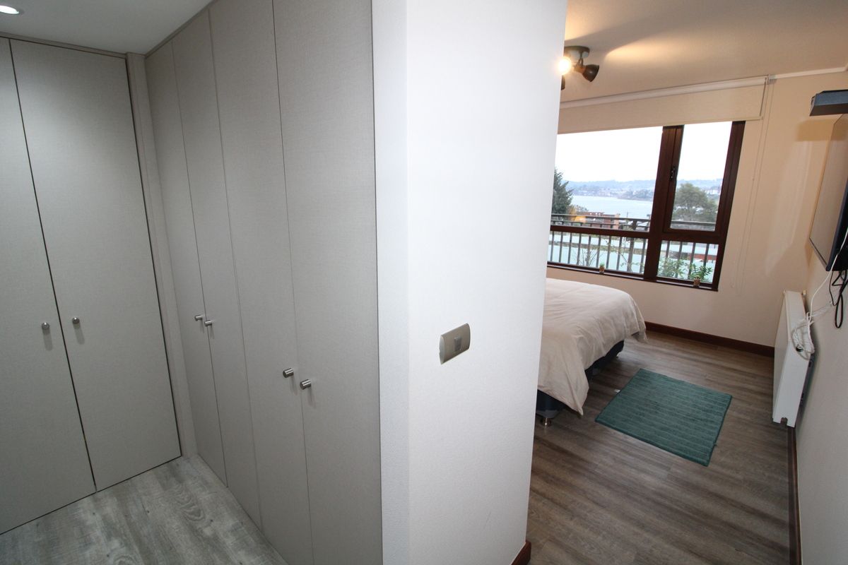Une chambre avec une grande armoire, un lit, une fenêtre donnant sur un beau paysage et un petit tapis vert.