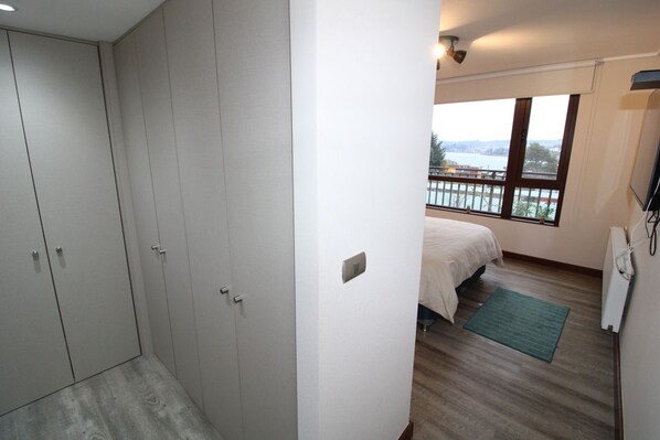 A bedroom with a large wardrobe, a bed, a window with a view, and a small green rug.