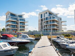 Un port de plaisance avec des immeubles d’appartements modernes, des bateaux amarrés et une promenade en bois.