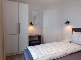 Un dormitorio con cama, armario, mesita de noche, espejo y lámpara de pared.
