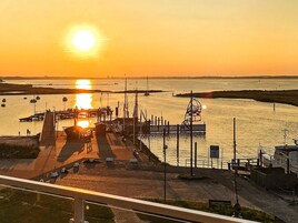 Una marina frente al agua con barcos amarrados, un paseo peatonal y un puente al fondo.