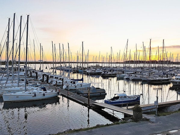 Uma marina com vários barcos atracados, um cais de madeira e água calma refletindo os barcos.