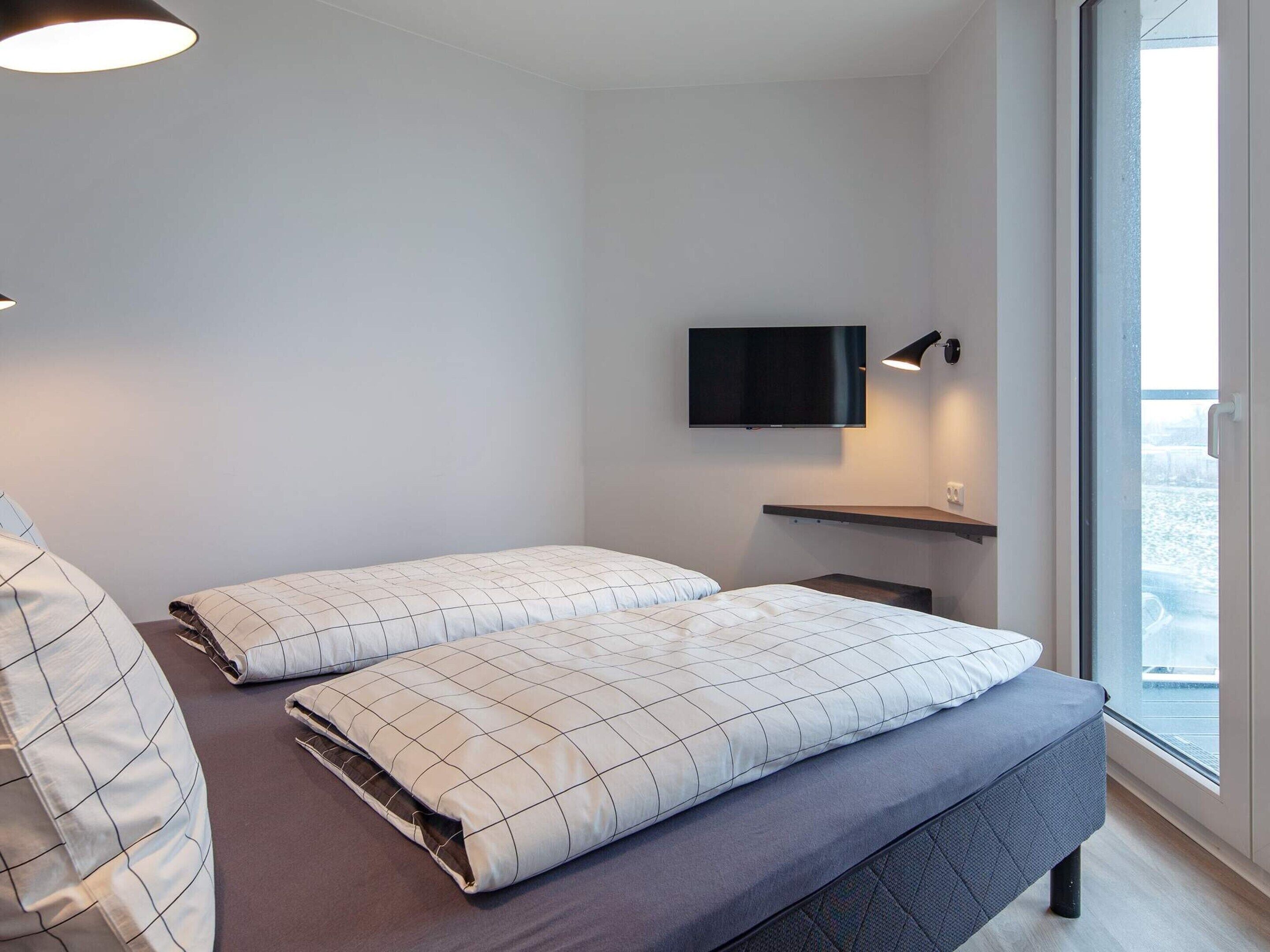 Habitación de hotel moderna con cama, televisor de pantalla plana en la pared y ventana con vistas al exterior.