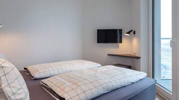Habitación de hotel moderna con cama, televisor de pantalla plana en la pared y ventana con vistas al exterior.