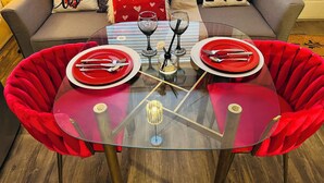 Un comedor con una mesa de vidrio, dos sillas rojas y un sofá con almohadones con forma de corazón.