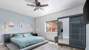 Un dormitorio moderno con cama, ventilador de techo, obras de arte y un ventanal grande.
