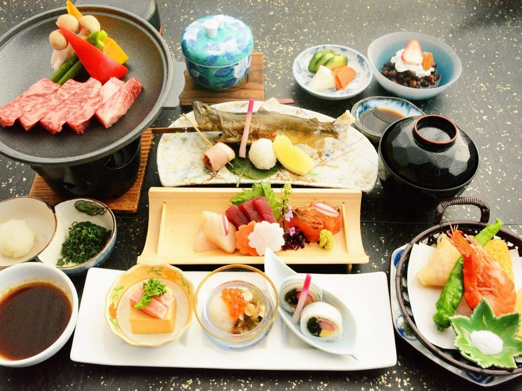 A variety of Japanese dishes including sushi, sashimi, and tempura, arranged on a table with a black tablecloth.