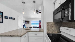 A kitchen with white cabinets, a granite countertop, a black microwave, and a stove. - Beachfront 1BR · Ocean View, Pool + Free Parking (Hollywood)