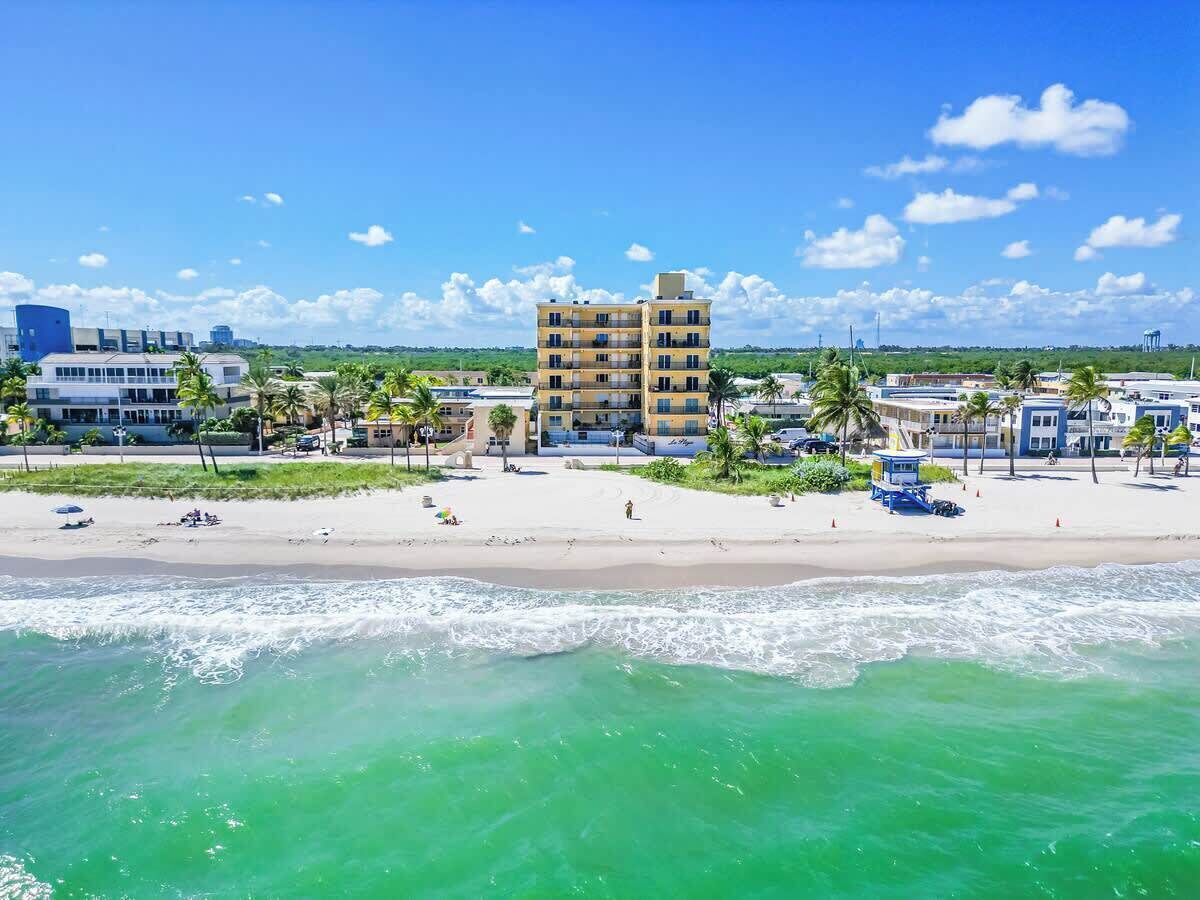 A beach with a hotel in the background, palm trees, and clear skies.