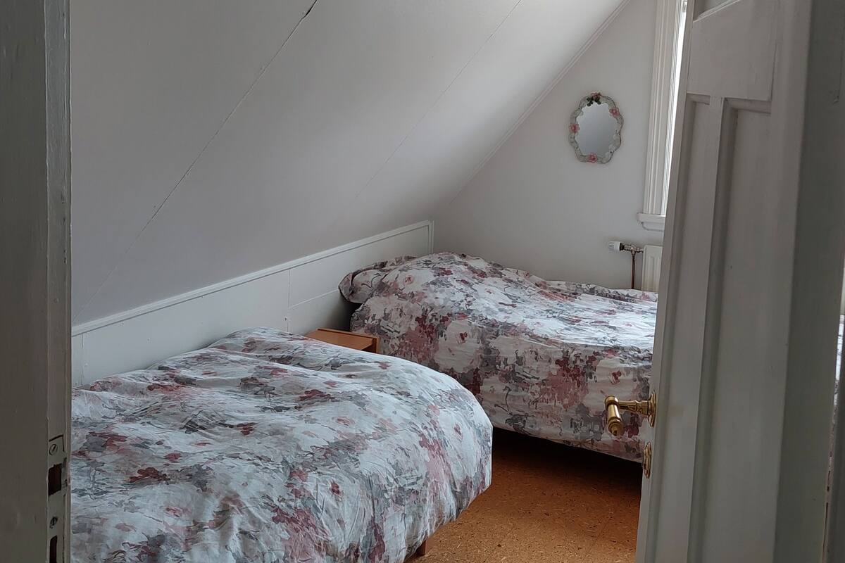 Een slaapkamer met twee eenpersoonsbedden, een deur en een klein raam.