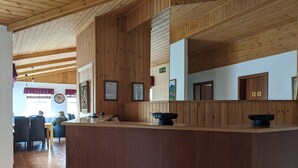 Een houten receptiebalie met een betegelde vloer, ingelijste foto’s aan de muur en een duidelijk zichtbaar vluchtbord.