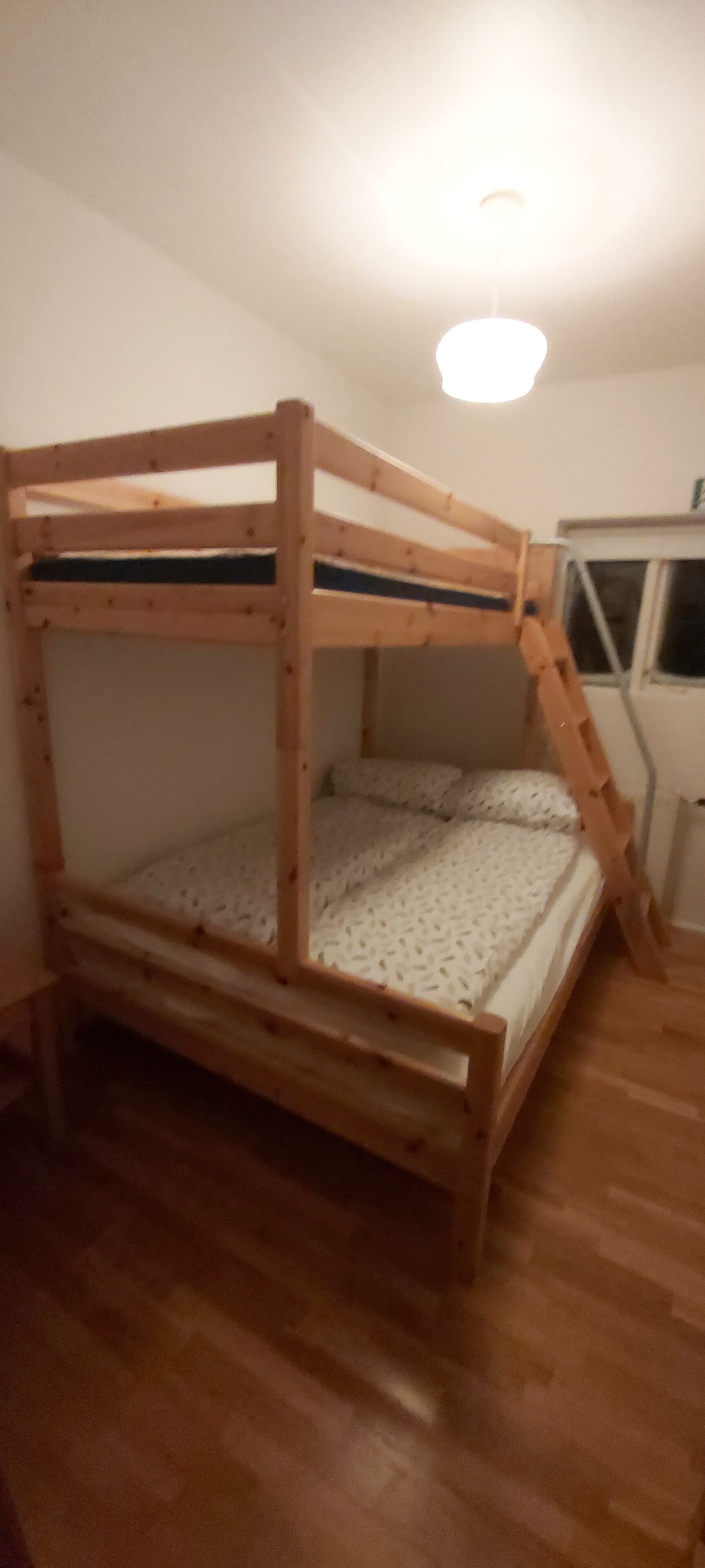 Una litera con escalera, suelo de madera y una ventana.