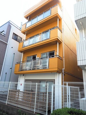 A multi-story residential building with balconies, a gated entrance, and a white fence.
