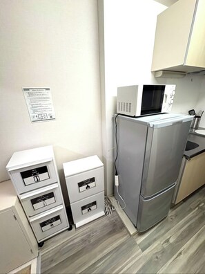 A compact kitchenette with a microwave, a refrigerator, and a small sink. There are three storage drawers with labels.