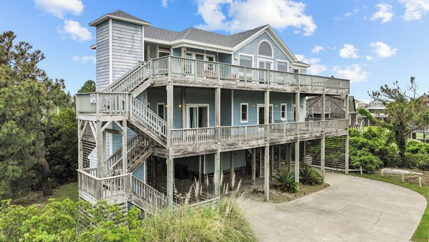 A two-story house with a balcony, a covered porch, and a concrete driveway. - 7135-Our Blue Haven - Waves Retreat | Pool | 300 Yards to Beach (Waves)