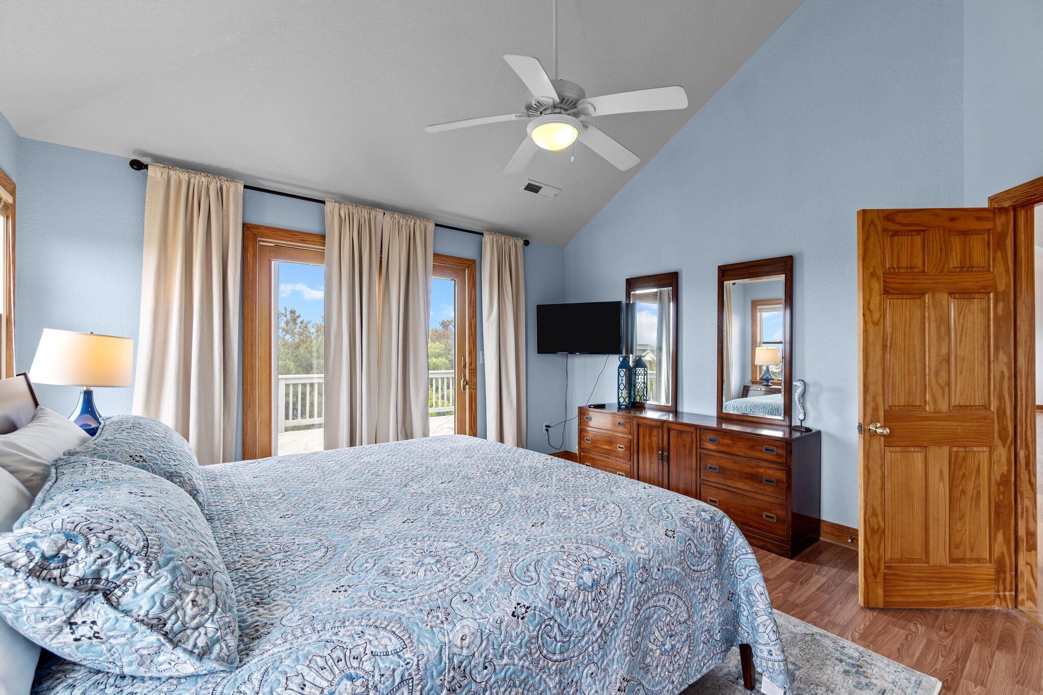 Ein Schlafzimmer mit Bett, Deckenventilator, Kommode, Fernseher und einer Tür.