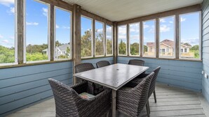A covered patio with a table and wicker chairs, large windows, and a view of houses. - 7135-Our Blue Haven - Waves Retreat | Pool | 300 Yards to Beach (Waves)