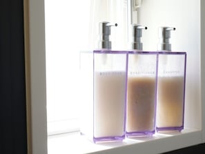 Drei Flaschen Duschgel, Conditioner und Shampoo auf einem Fensterbrett.