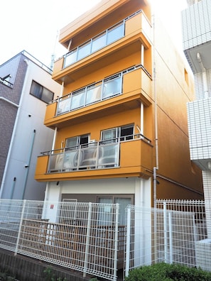 A multi-story residential building with balconies, a gated entrance, and a white fence.