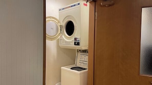 A compact laundry room with a front-loading washer and dryer, a control panel, and a door.