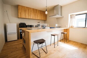 A compact kitchen with wooden cabinets, a built-in island with stools, a refrigerator, and a window with curtains. - A treasure trove of experiences and fun  Baby go / Hokuto Yamanashi (Hokuto)