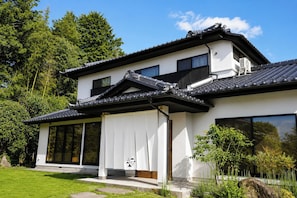 Une maison moderne à deux étages, dotée d’un toit traditionnel recouvert de tuiles, de grandes fenêtres et d’un jardin bien entretenu.