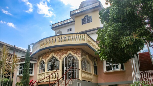 A two-story house with a curved balcony, a staircase, and a small garden area. - Van Villa Holidays (Negril)