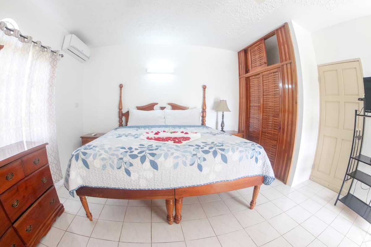 Quarto com cama de madeira, penteadeira, ar-condicionado, guarda-roupa e apoio para TV.