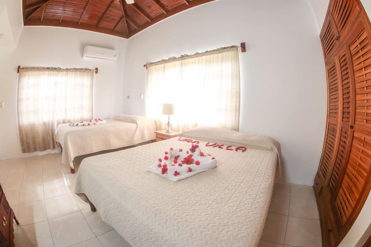 Quarto de hotel com duas camas, teto de madeira e janela com cortinas.
