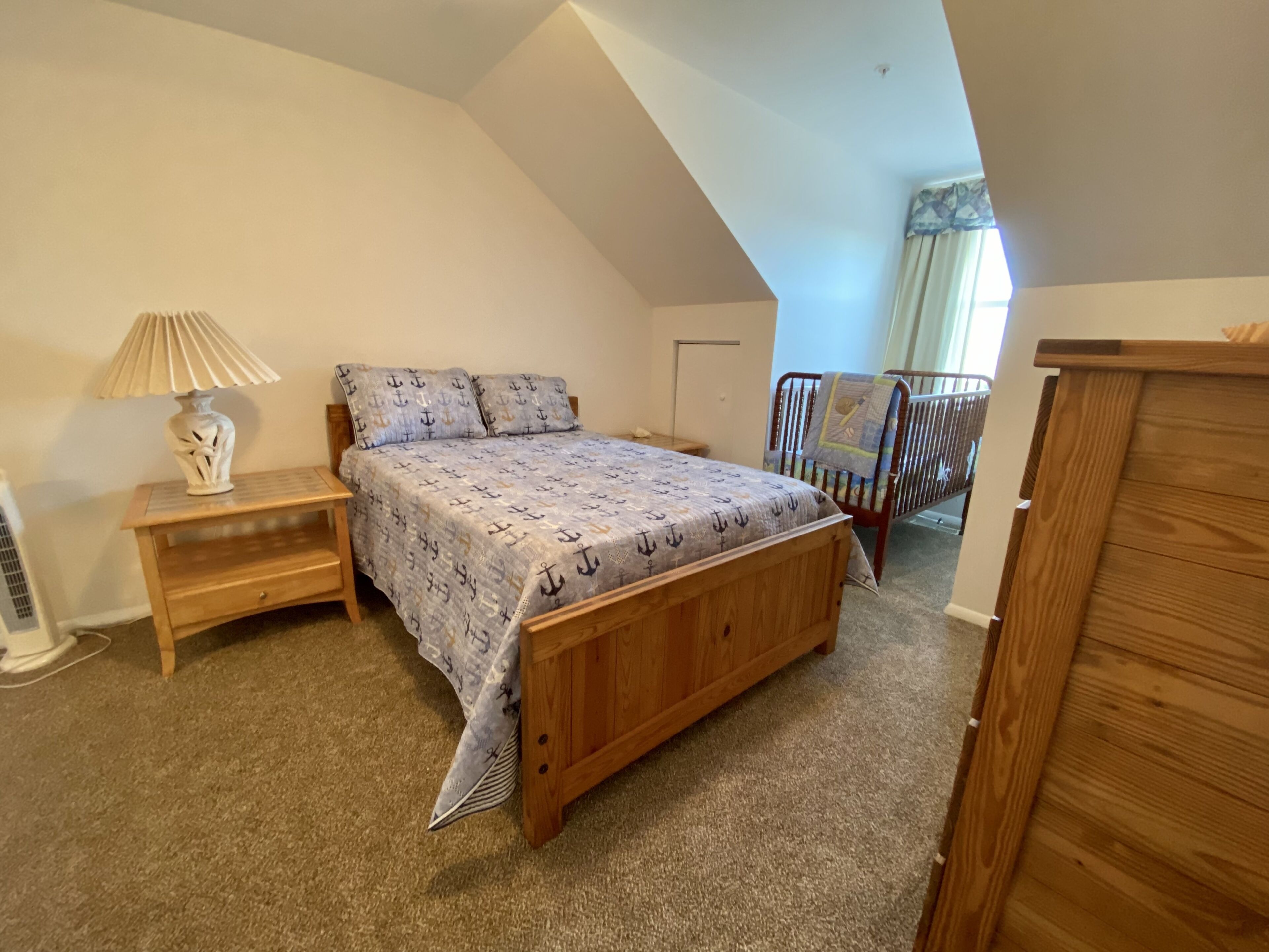 Ein Schlafzimmer mit schrägverdeckter Decke, einem Holzbett, einem Nachttisch, einer Lampe und einer Kommode.