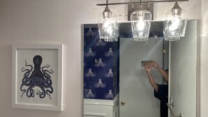 A bathroom with a framed octopus artwork, a blue patterned shower curtain, and three pendant lights above the mirror. - Bethany Bay Beach Oasis, 4 Bed 3 bath, pool, golf, kayak, Ocean View (Ocean View)