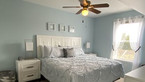 A bedroom with a bed, nightstands, a ceiling fan, and a window with curtains. - Bethany Bay Beach Oasis, 4 Bed 3 bath, pool, golf, kayak, Ocean View (Ocean View)