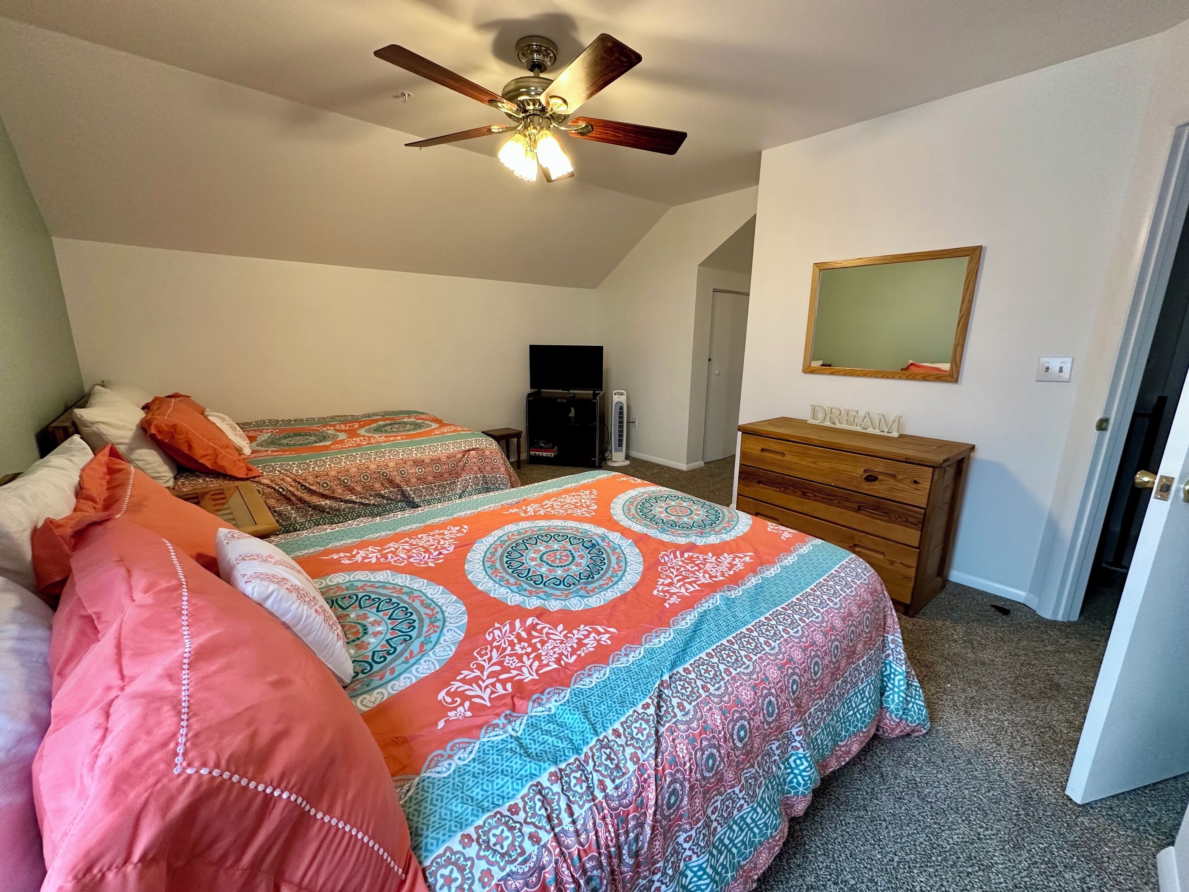 A bedroom with two beds, a ceiling fan, a dresser, and a television.