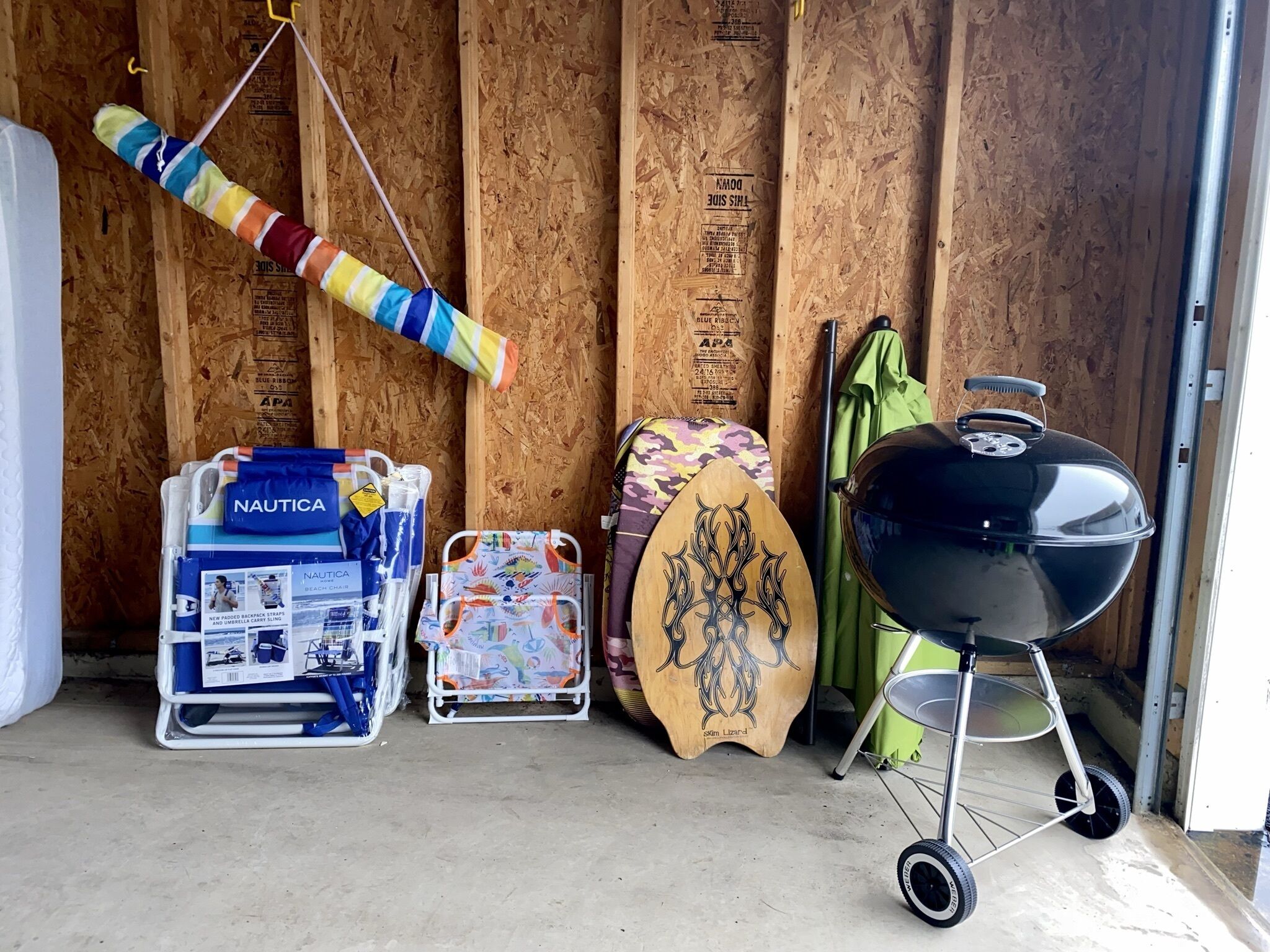 Eine Garage mit Holzwand, einer bunten Hängematte, einem Grill, einem Surfbrett und einem Liegestuhl.