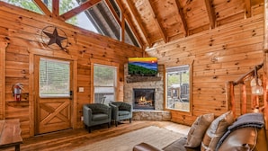 A cozy cabin interior with a stone fireplace, two armchairs, a leather sofa, and a star decoration on the wall. - Grand Mountain View Lodge By Ghosal Lodging (Sevierville)