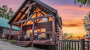 A log cabin with a welcoming sign, a porch with chairs, and a view of the sunset. - Grand Mountain View Lodge By Ghosal Lodging (Sevierville)