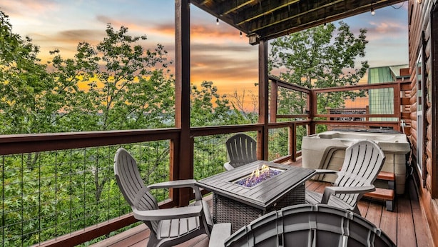 A covered outdoor deck with a table and chairs, overlooking a garden and buildings. - Grand Mountain View Lodge By Ghosal Lodging (Sevierville)