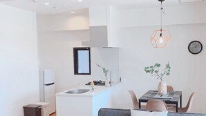 Eine moderne Küche mit weißen Schränken, einem eingebauten Backofen und einer Spüle. Es gibt eine Essecke mit Tisch und Stühlen sowie ein graues Sofa mit Kissen.