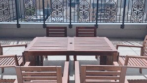 Ein Balkon mit Holztisch und -stühlen, einem dekorativen Geländer und Blick auf die Stadt.