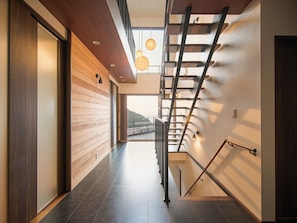 Un interior moderno con una pared de madera, una escalera con barandillas metálicas e iluminación colgante.