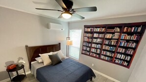 A bedroom with a bed, a ceiling fan, a bookshelf, and a window with blinds.