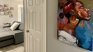 A room with a grey sofa, a white door, and a colorful abstract painting on the wall.