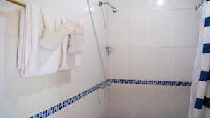 A bathroom with white tiled walls, a shower with a blue-tiled border, and a white towel rack with towels and a bathrobe.