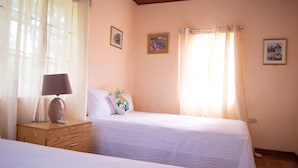 A bedroom with two beds, a nightstand, a lamp, and a window with curtains.
