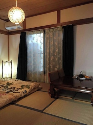 A traditional Japanese-style room with tatami flooring, a low wooden table, a bed with a floral bedspread, and a hanging light fixture.