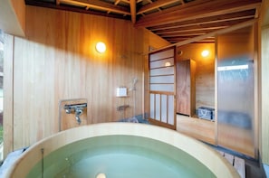 Relax in a traditional Japanese-style hot spring bath area with a large, oval-shaped hot tub and wooden bench.