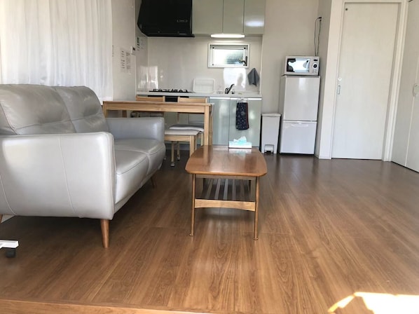 Un espace de vie compact comprenant un canapé en cuir gris, une table basse en bois et un petit coin cuisine équipé d’une cuisinière, d’un four à micro-ondes et d’un réfrigérateur.