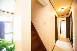 A hotel hallway with a wooden staircase, a light fixture, and a door at the end.