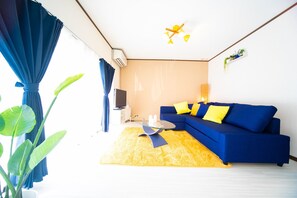 Ein modernes Wohnzimmer mit einem blauen Sofa, gelben Kissen, einem Glastisch und einem gelben Teppich.