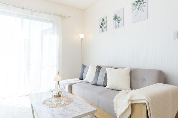 A living room with a sofa, a coffee table, a lamp, and framed botanical prints on the wall.